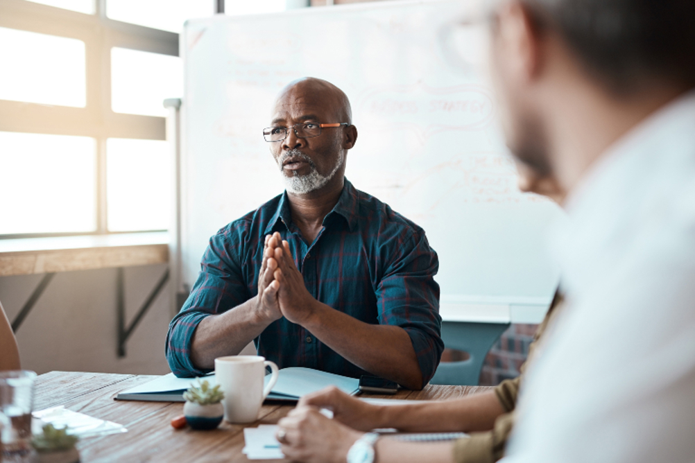 A black male social worker (or other professional) addressing a meeting around a table