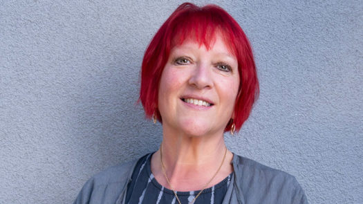 Andrea Egan, a red-haired woman, wearing a grey cardigan and stripy to