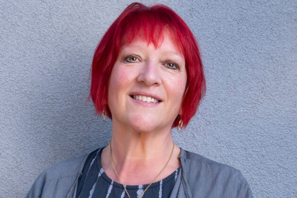 Andrea Egan, a red-haired woman, wearing a grey cardigan and stripy to