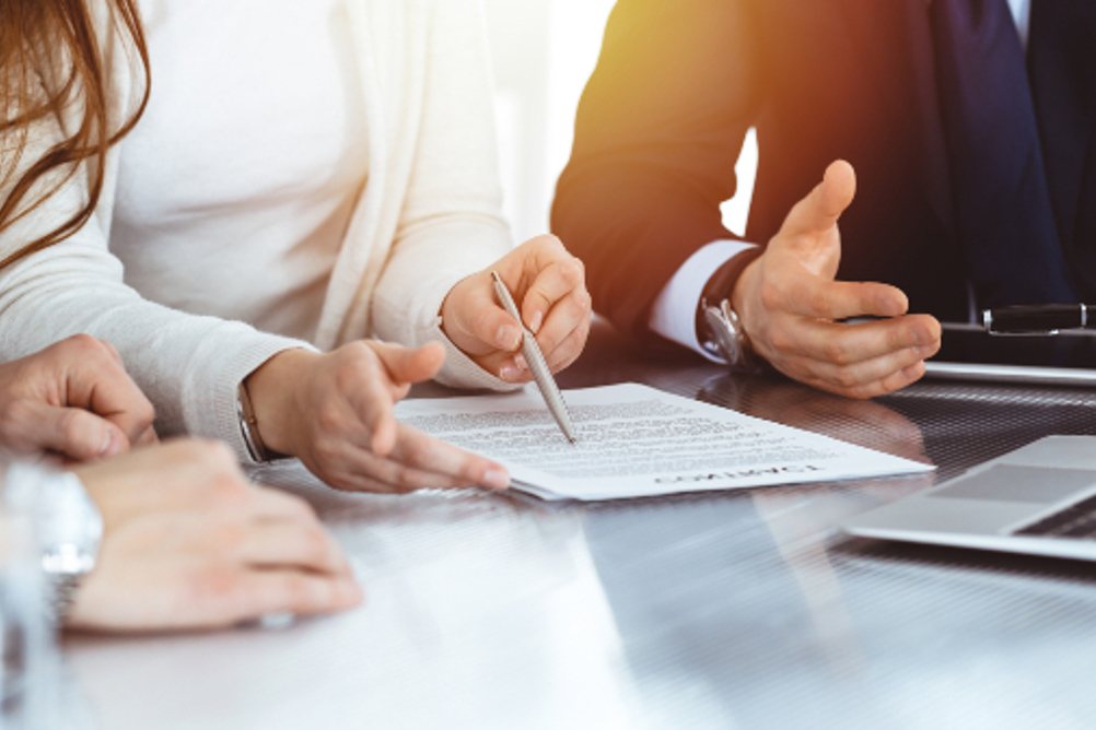 Two Men And A Woman Involved In A Negotiation Meeting Discussing A Document That Is On A Table In Front Of Them
